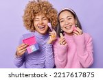 Positive mixed race women apply foundation and colorful palette do makeup want to look beautiful dressed casually have positive expressions isolated over purple background. Cosmetology concept