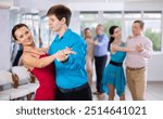 Positive modern young guy and woman dancing slow ballroom dance during group class in choreography studio..