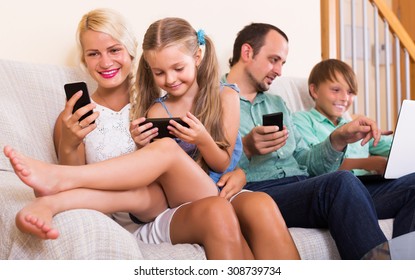 Positive Mom, Dad And Two Happy Kids Working With Smartphones Indoors