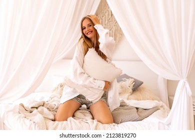 Positive Morning Portrait Of Pretty Blonde Woman Wearing Pijama And Having Fun At Her Boho Style Bedroom. Home Office Time.