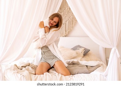 Positive Morning Portrait Of Pretty Blonde Woman Wearing Pijama And Having Fun At Her Boho Style Bedroom. Home Office Time.