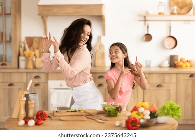 Positive mother and kid daughter dancing and enjoying while preparing dinner in modern kitchen indoor, having fun and sharing joyful moments during salad making. Family Leisure and Nutrition - Powered by Shutterstock