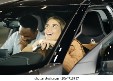 Positive Multi Ethnic Couple Examining Modern Car At Showroom Before Making Purchase. African Man And Caucasian Woman Buying New Vehicle At Auto Salon.