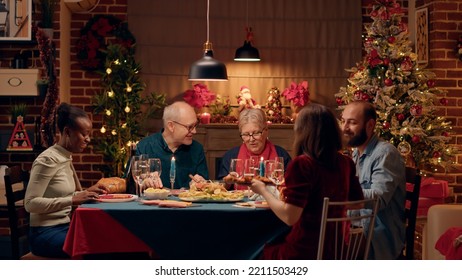 Positive multicultural family members celebrating Christmas with special evening dinner at home. Happy people enjoying traditional home cooked food while having a good time together. Tripod shot - Powered by Shutterstock