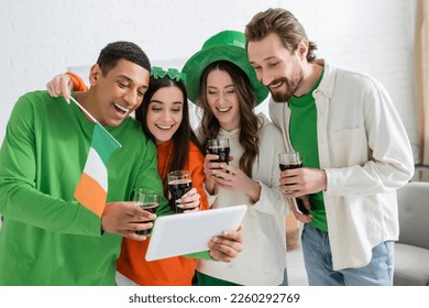 Positive multiethnic friends with beer celebrating saint patrick day and using digital tablet at home  - Powered by Shutterstock