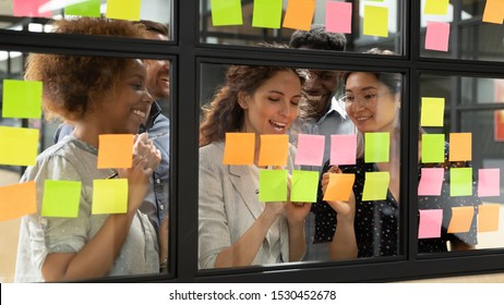 Positive multi-ethnic group of business people working together on new project writing main topics sharing creative ideas thoughts using colourful post-it sticky notes, concept of synergy and teamwork