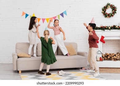 Positive Multiethnic Kids Playing Tag Near Christmas Decor In Living Room