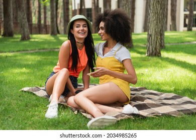 Positive Multiethnic Same Sex Couple Sitting On Blanket In Park