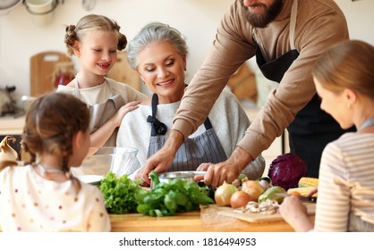 Positive Multigenerational Family Gathering In Home Kitchen And Preparing Delicious Healthy Food With Fresh Vegetables For Lunch Together
