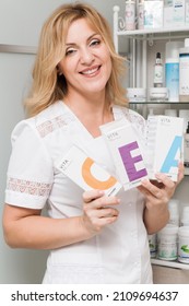 Positive Nice Mature Beautician Stands In Her Cabinet With With Cosmetic Packaging In  Hands And Pose And Looks At Camera. - Minsk, Belarus - September 25, 2021