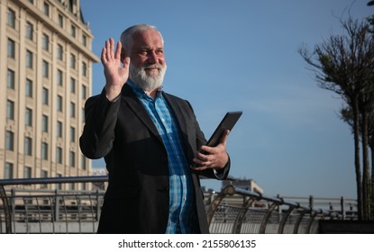 Positive Old Bearded Man Looking Into The Distance And Waving Goodbye While Holding A Tablet