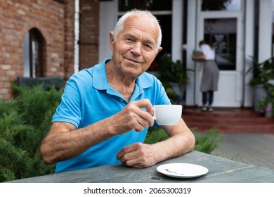 Positive Old Man Sitting At Table In Outdoor Cafe And Drinking Tea.