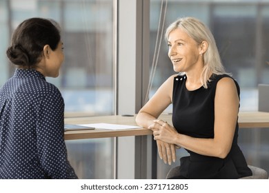 Positive older and younger office colleagues discussing work process, job tasks, cooperation, sitting at coworknig desk, collaborating on project, enjoying professional networking - Powered by Shutterstock