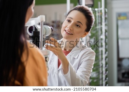 positive ophthalmologist pointing with hand near blurred woman and vision screener