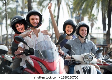 Positive Parents And Adult Children 20-30 Years Old Traveling Through City By Scooters