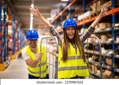 Positive People Having Fun At Work. Warehouse Workers Pushing Carts And Enjoying In Storage Room.