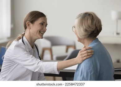 Positive physician woman talking to elderly patient, touching shoulder, smiling, giving support, comfort, medical advice. Senior lady visiting doctor for medical examination - Shutterstock ID 2258472337