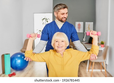 Positive physiotherapist helping a senior woman to lift dumbbells for rehabilitation after injury. Physio treatment at a rehab center