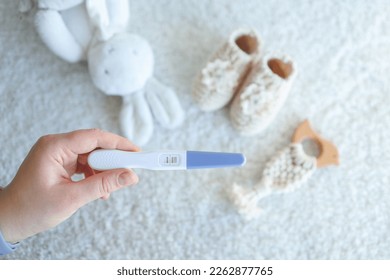 Positive pregnancy test in hand against the background of children's clothing.