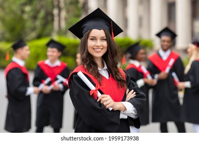 Positive Pretty Young Lady Student Having Graduation Party, Wearing Graduation Costume And Holding Diploma, Happy Female Graduate Proudly Posing At University Campus, Blurred Background