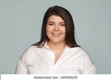 Positive Reaction, Attitude And Life Perception. Cute Charming Young Caucasian Woman With Curvy Body Posing At Gray Office Wall And Smiling Cheerfully At Camera, Rejoicing At Her Career Success