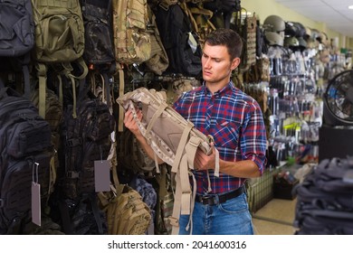 Positive Russian Man Choosing Textile Backpack Gun In Military Shop