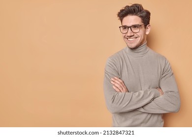 Positive self confident man keeps arms folded looks away with satisfied expression listens good news wears spectaces and casual turtleneck isolated over beige background blank space for promo - Shutterstock ID 2132847321