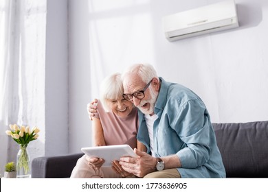 Positive senior coupe using digital tablet on couch at home