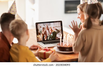 Positive senior couple grandparents wearing party hats congratulating little girl online via video call on laptop, waving at camera and blowing whistles, child celebrating birthday with family at home - Powered by Shutterstock