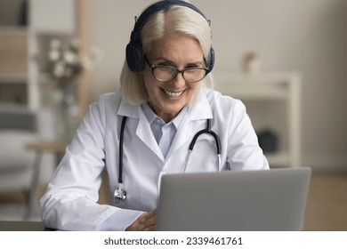 Positive senior doctor woman in wireless headphones speaking on online video call to patient, giving assistance, consultation, phone support. Medical expert giving webinar, lecture on Internet - Powered by Shutterstock