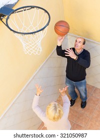 Positive Senior Family Couple Playing Basketball In Patio