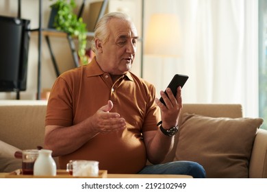 Positive Senior Man Sitting On Couch At Home And Video Calling His Best Friend Or Family Member