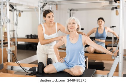 Positive senior woman doing exercises on reformer in pilates studio with young female personal trainer controlling her movements.. - Powered by Shutterstock