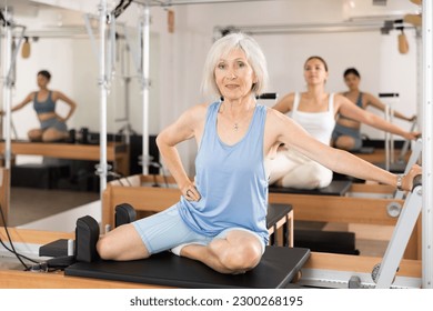 Positive senior woman doing stretching exercises on pilates reformer as part of injury rehabilitation course. Therapeutic physical training concept - Powered by Shutterstock