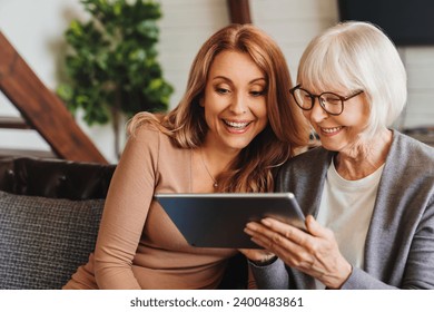 Positive senior woman and her daughter using tablet at home. Woman granddaughter teaching granny how to use gadgets, helping with paying domestic bills, pension, e-banking - Powered by Shutterstock