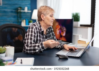 Positive Senior Woman Paying Bills Holding Plastic Credit Card. Joyful Elderly Woman Using Online Banking For Payment Transcation Surfing On Internet From Home Living Room.