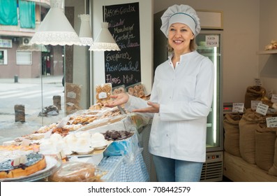 Positive Senior Woman Selling Nuts And Pastry In Shop