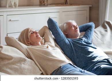 Positive Serene Mature Couple Wearing Casual Clothing Lying On Comfy Sofa Putting Hands Behind Heads Sleeping Or Daydreaming. Middle Aged Spouses Wife Husband Resting In Sitting Room Having Day Nap