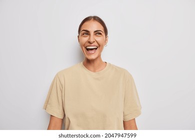 Positive Sincere Young European Woman Smiles Gladfully Has Upbeat Mood Laughs At Something Dressed In Casual Beige T Shirt Isolated Over White Background. Human Emotions And Feelings Concept