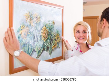 Positive Smiling Couple Hanging Art Picture In Frame On The Wall