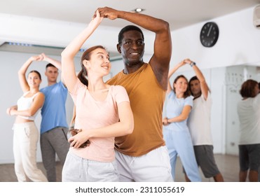 Positive smiling dancing couple enjoying active dancing during group training in dance hall - Powered by Shutterstock