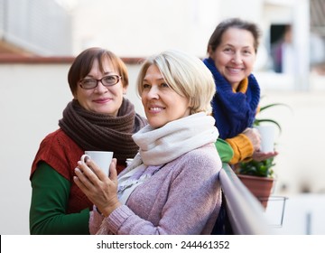 Positive Smiling Elderly Female Friends Drinking Coffee At Patio. Focus On Blonde 