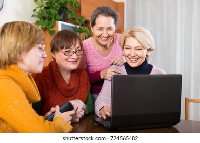 Positive smiling female pensioners browsing web on laptop at home