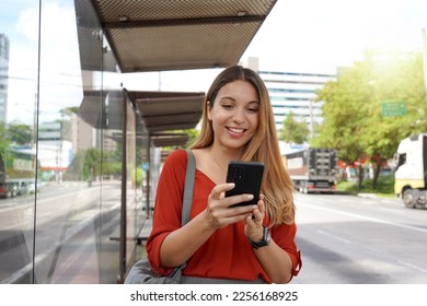 Positive smiling girl buying ticket online with smartphone at bus stop - Powered by Shutterstock