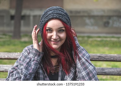 Positive smiling homeless red hair girl sitting on the bench on the street and looking in the camera  while she having fun, happy homeless concept