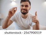 Positive smiling man is sitting holding pill, conception of medicine.