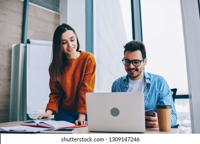 Positive smiling man and woman near working place with laptop cooperating in office, male and female employees collaborating on startup share ideas in friendly atmosphere using wireless for research