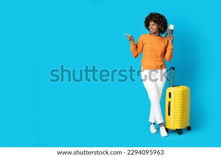 Positive smiling pretty young african american woman wearing comfy casual outfit with yellow luggage tourist pointing at copy space, holding passport and flight tickets, showing nice deal