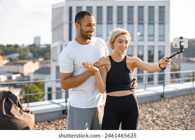 Positive sports couple of bloggers tells their followers how to properly perform exercises to maintain healthy lifestyle. Sporty man and woman writing blog using phone on rooftop. - Powered by Shutterstock