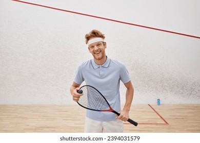 positive sportsman in sportswear holding squash ball and racquet while standing inside of court - Powered by Shutterstock